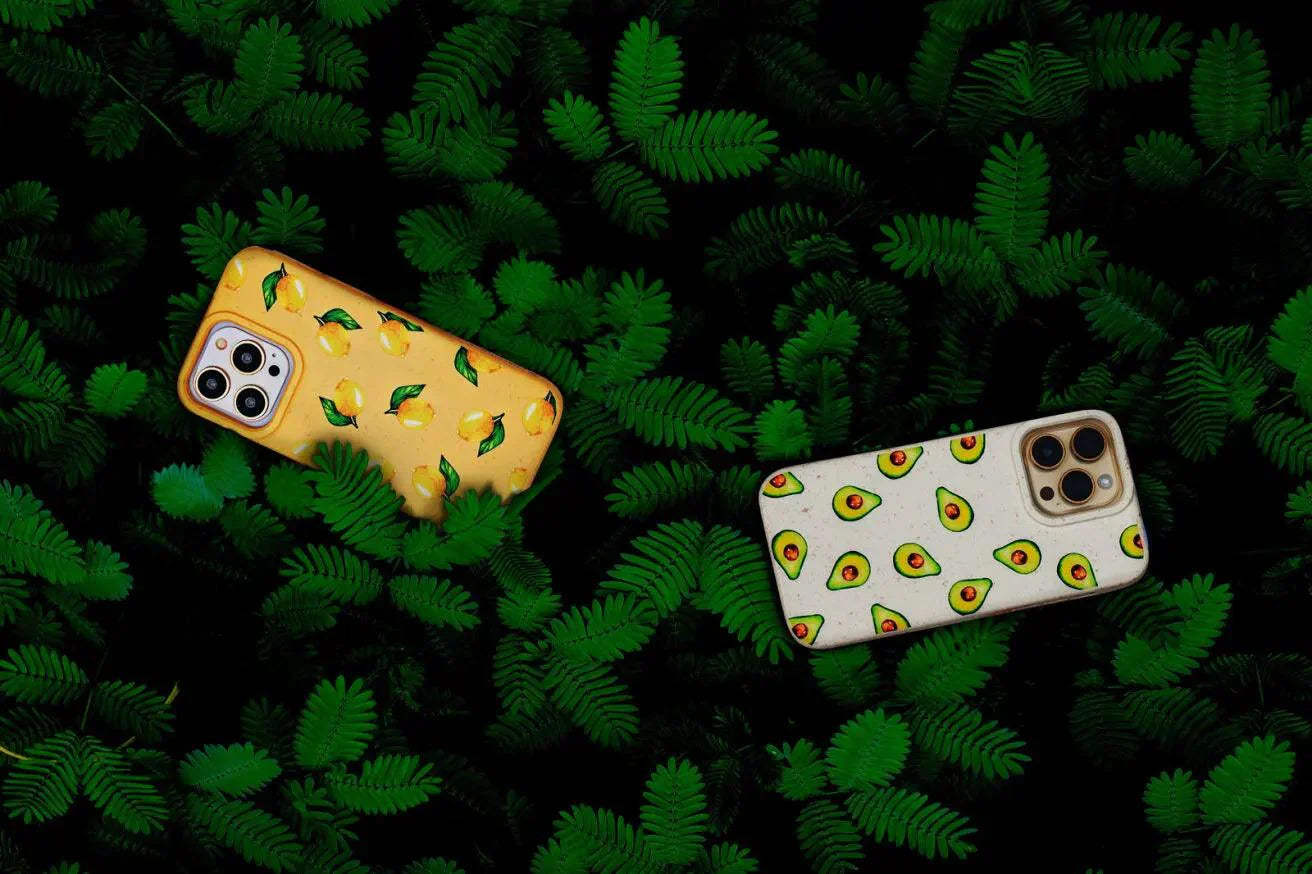 A pile of green leaves with two eco-friendly phone cases on top. The phone cases have lemon and avocado designs.